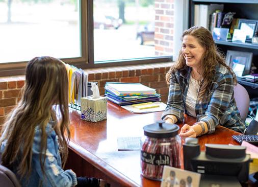 advisor talks to student while sitting at desk